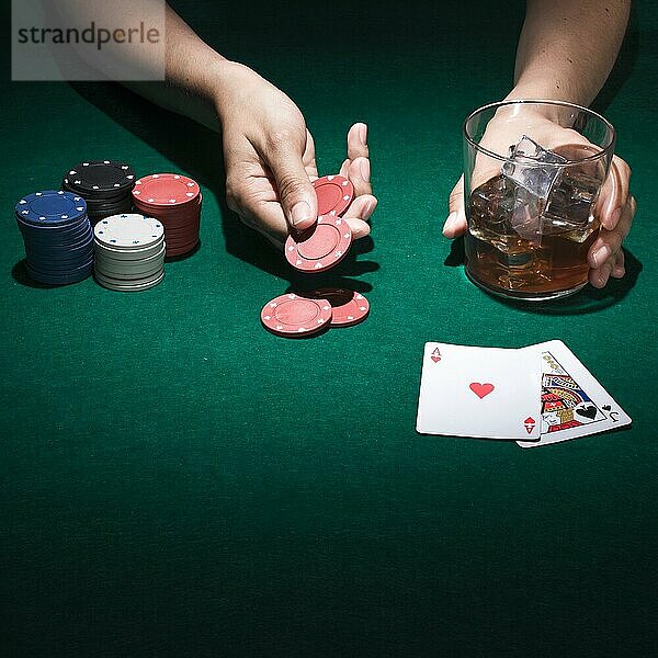 Person  die ein Glas Whiskey hält  während sie eine Pokerkarte spielt