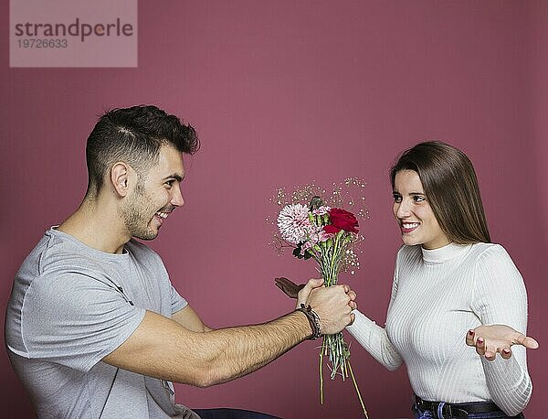 Lächelnder Mann präsentiert frische Blumen überrascht attraktive Dame