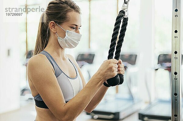 Seitenansicht Frau mit medizinischer Maske beim Training im Fitnessstudio während der Pandemie