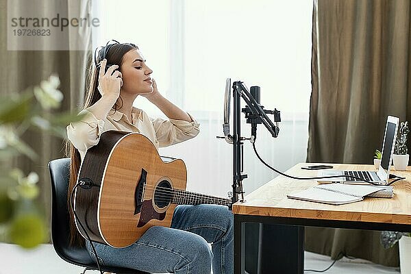 Seitenansicht einer Musikerin  die Akustikgitarre spielt und einen Song zu Hause aufnimmt