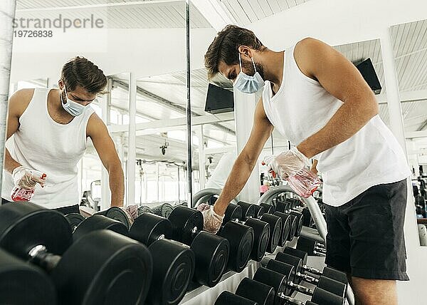 Seitenansicht Mann desinfiziert Fitnessgeräte und trägt dabei eine medizinische Maske