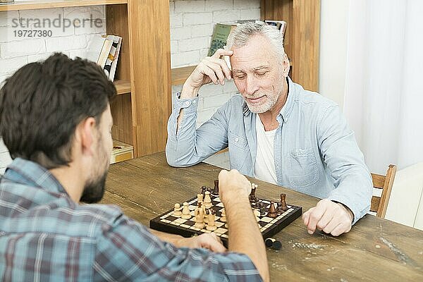 Pensive im Alter von Mann junger Mann spielt Schach Tisch in der Nähe von Bücherregalen