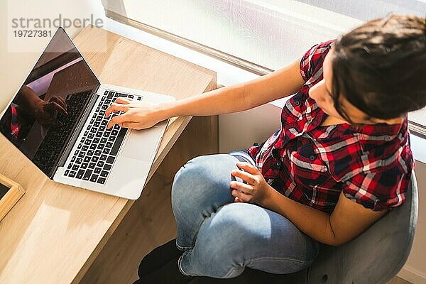 Draufsicht auf eine Frau  die von zu Hause aus mit einem Laptop auf einem Schreibtisch arbeitet