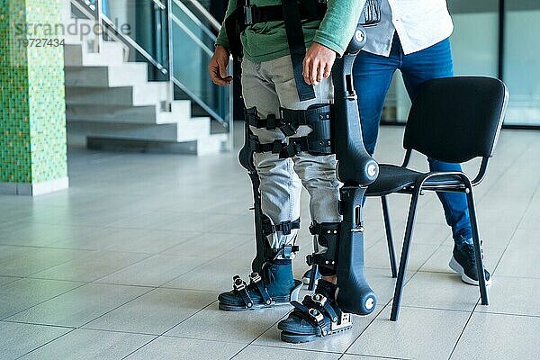 Mechanisches Exoskelett  Physiotherapeutin hilft behinderter Person mit Roboterskelett aufzustehen  Physiotherapie in einem modernen Krankenhaus: