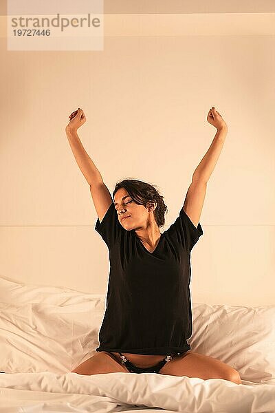 Vertikales Foto einer Frau  die morgens auf dem Bett sitzend die Arme ausstreckt
