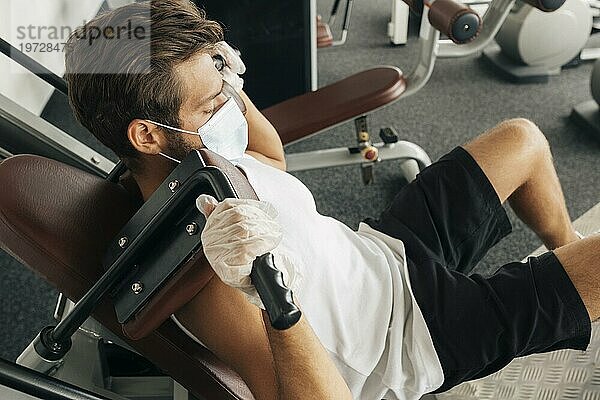 Mann mit medizinischer Maske an Fitnessgeräten
