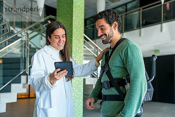 Mechanische Exoskelett  weibliche Physiotherapeut Arzt im Gespräch und lächelnd mit Tablet mit behinderter Person mit Roboterskelett Physiotherapie in modernen Krankenhaus  futuristische Physiotherapie