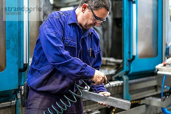 Fabrikarbeiter im Bereich der numerischen Steuerung  der ein Teil mit Druckluft reinigt  Metallindustriewerk