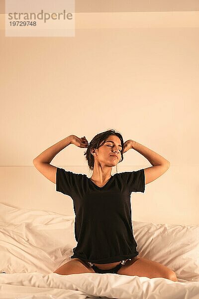 Vertikales Foto einer Frau  die sich morgens auf dem Bett sitzend streckt