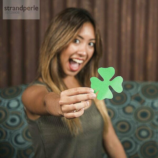 Weinende glückliche Frau mit grünem Papierklee in der Hand