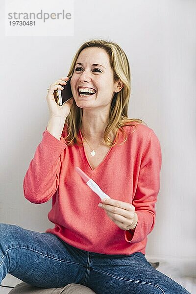 Fröhliche Frau mit Schwangerschaftstest beim Telefonieren