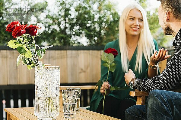 Lächelnde schöne junge Frau hält rote Rose im Gespräch mit seinem Freund