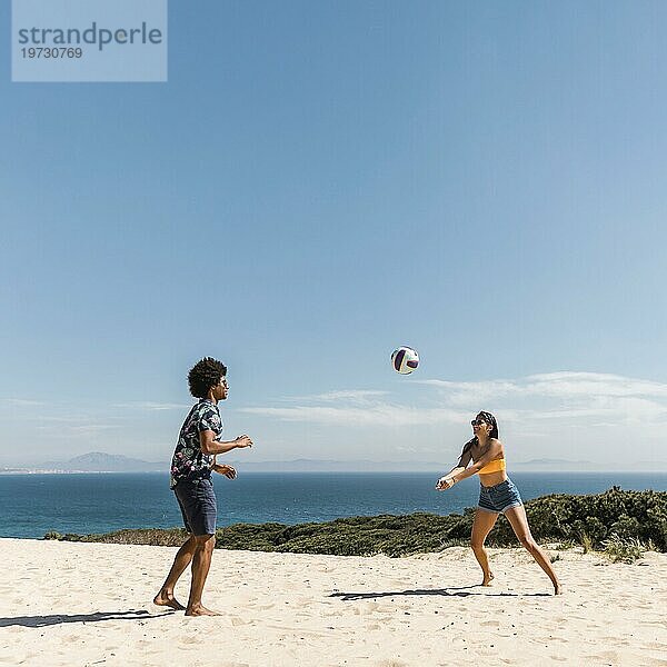 Junges multikulturelles Paar spielt Volleyball am Strand