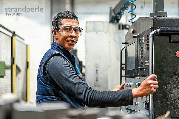 Porträt eines lateinischen Industriearbeiters in der Metallindustrie im Bereich der numerischen Steuerung  der die Tasten auf dem Bedienfeld berührt