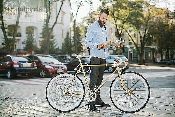 Fröhlicher Mann liest Zeitung in der Nähe des Fahrrads