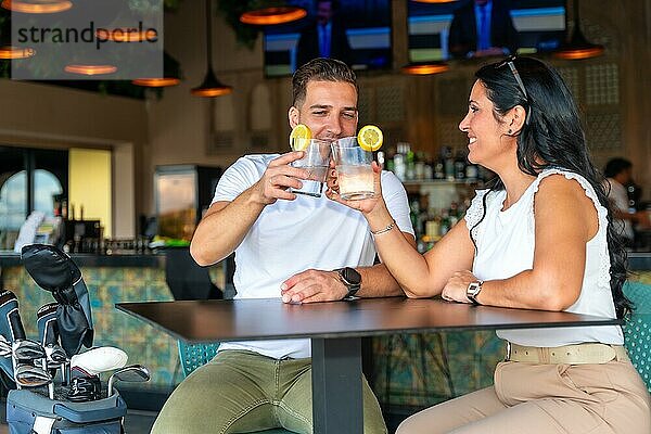 Paar stößt mit Cocktails im Restaurant eines Golfclubs an