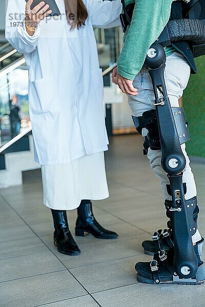 Mechanische Exoskelett  weibliche Physiotherapeut Arzt im Gespräch und lächelnd mit Tablet mit behinderter Person mit Roboterskelett Physiotherapie in modernen Krankenhaus  futuristische Physiotherapie