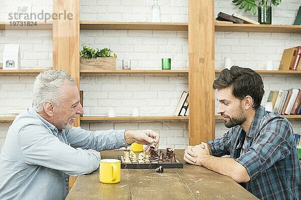 Glücklicher älterer Mann junger Mann spielt Schach Tisch Zimmer