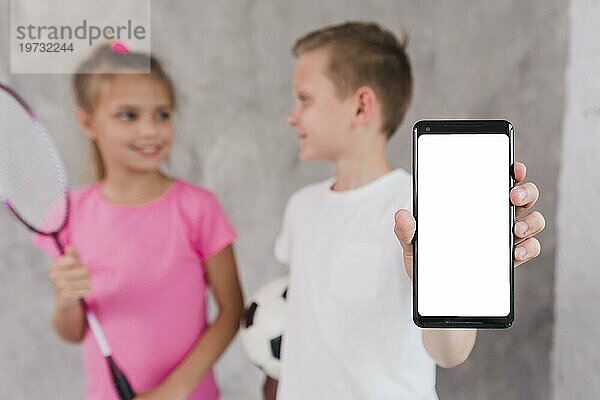 Junge stehend mit Mädchen  das ein Mobiltelefon mit weißem Bildschirm zeigt
