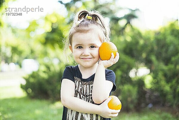 Lächelndes Mädchen hält zwei frische Orangen im Park