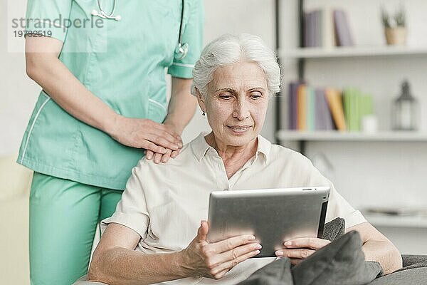 Krankenschwester steht neben einer älteren Frau und benutzt ein digitales Tablet