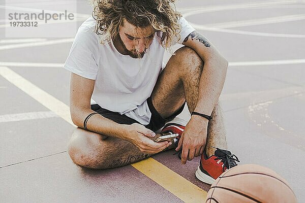 Basketballspieler auf dem Platz  der ein Mobiltelefon benutzt