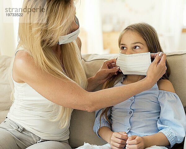Mutter hilft Tochter beim Anlegen der medizinischen Maske