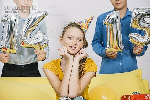 Porträt schöne lächelnde Mädchen sitzen vor Jungen halten Zahl 14 15 Folienballons