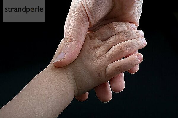 Erwachsener und Kind halten Hände in schwarzem Hintergrund