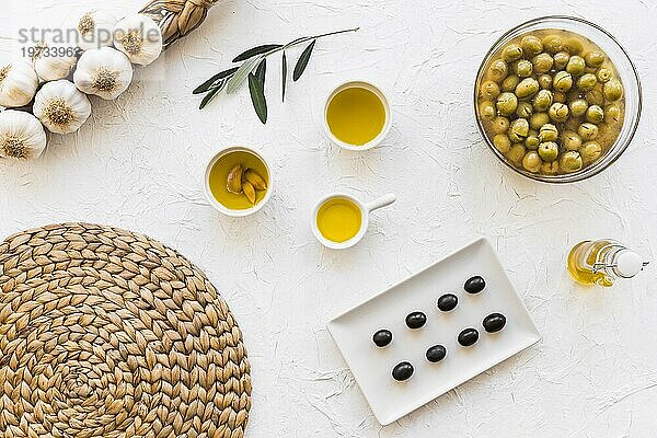 Olivenöle mit Bündel Knoblauchzwiebeln Untersetzer weißer Hintergrund