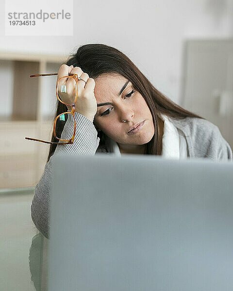 Frau arbeitet am Laptop und hält eine Brille