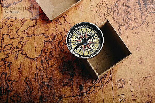 Kompass auf alter Landkarte neben einer Schachtel als Konzept des Reisens