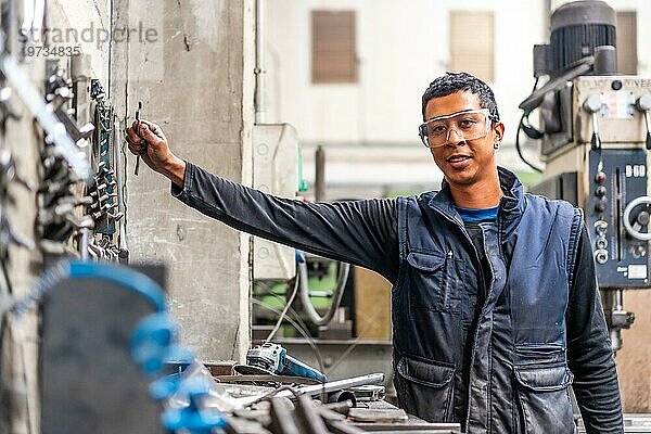 Latino Arbeiter in der Metallindustrie im Bereich der numerischen Steuerung  der Werkzeuge aufhebt