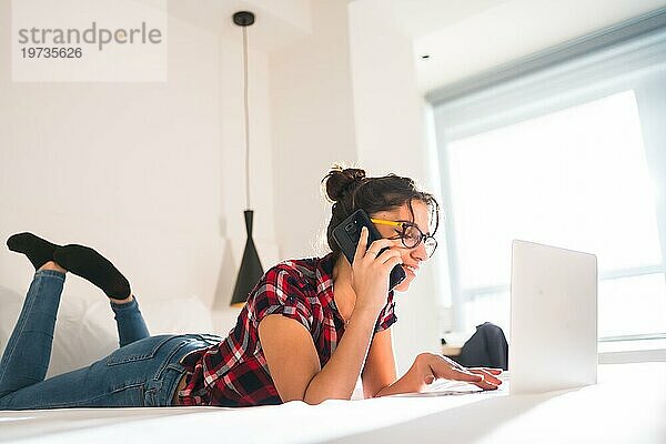 Seitenansicht einer jungen Frau  die mit dem Handy spricht  während sie in einem Hotelzimmer arbeitet