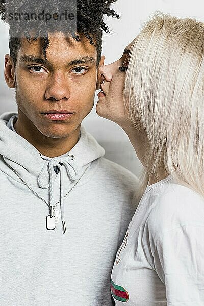 Blonde junge Frau küsst ihren ernsten afrikanischen Freund auf die Wange