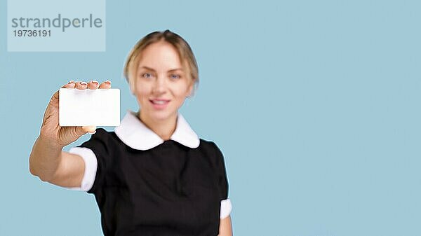 Defokussierte Frau zeigt leere weiße Visitenkarte vor blauem Hintergrund