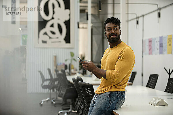 Afroamerikanischer Mann benutzt Smartphone  während er sich auf den Tisch lehnt