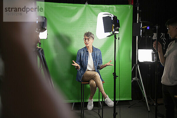 Eine Frau mittleren Alters gibt ein Interview  während sie vor einem grünen Bildschirm sitzt