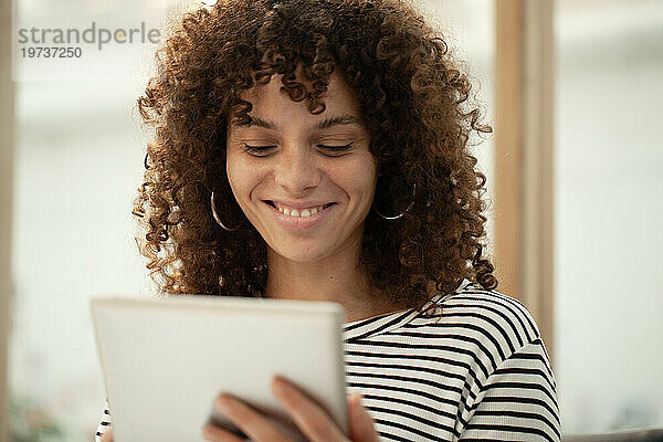 Junge erwachsene Frau lächelt  während sie ein digitales Tablet benutzt