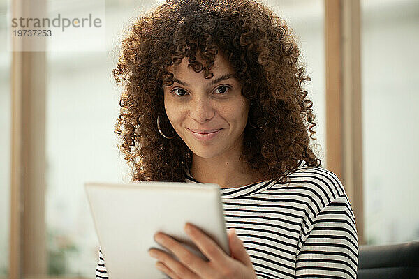 Junge erwachsene Frau schaut in die Kamera  während sie ein digitales Tablet benutzt