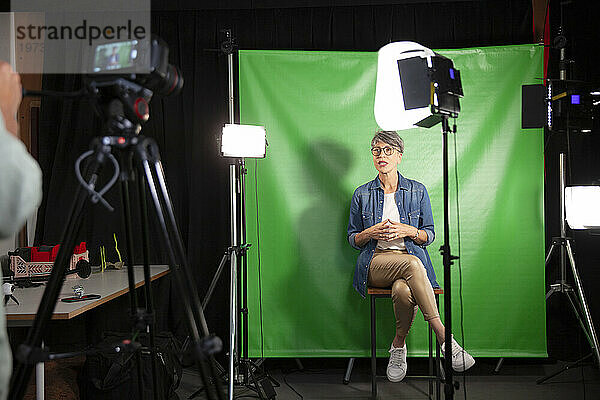 Eine Frau mittleren Alters gibt ein Interview  während sie vor einem grünen Bildschirm sitzt