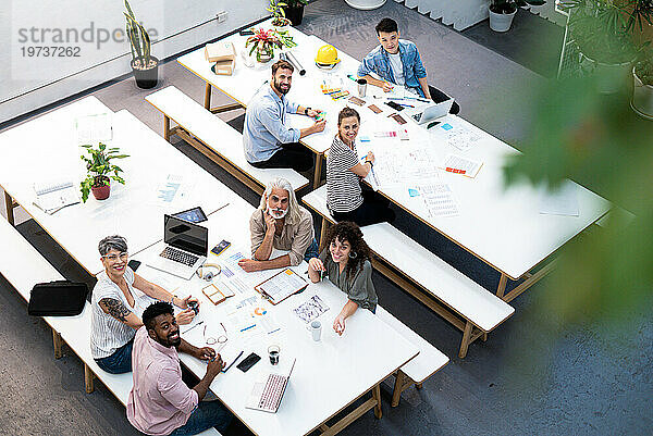 High angle view of coworkers looking at the camera while having a meeting at office