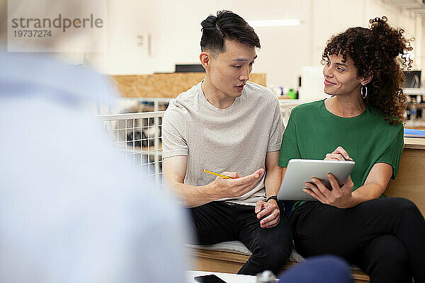 Kollegen diskutieren über ein digitales Tablet  während sie im Büro sitzen
