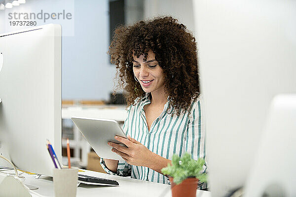 Junge erwachsene Geschäftsfrau nutzt digitales Tablet  während sie im Büro sitzt