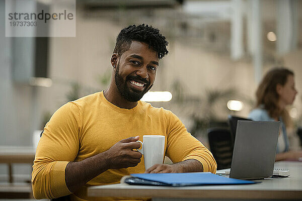 Afroamerikanischer Mann trinkt eine Tasse Kaffee  während er mit einem Laptop arbeitet