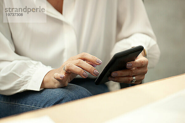 Mittlerer Teil einer Frau  die ihr Smartphone benutzt  während sie im Büro sitzt