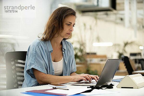 Erwachsene Grafikdesignerin benutzt Laptop  während sie am Schreibtisch sitzt