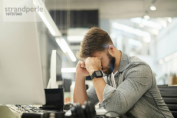 Gestresster männlicher Unternehmer sitzt am Schreibtisch und hat Kopfschmerzen