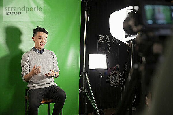 Junger erwachsener Mann gibt ein Interview  während er vor einem grünen Bildschirm sitzt