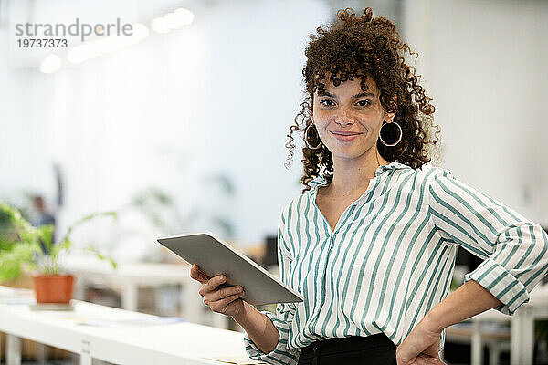 Selbstbewusste Geschäftsfrau hält ein digitales Tablet in der Hand und blickt in die Kamera